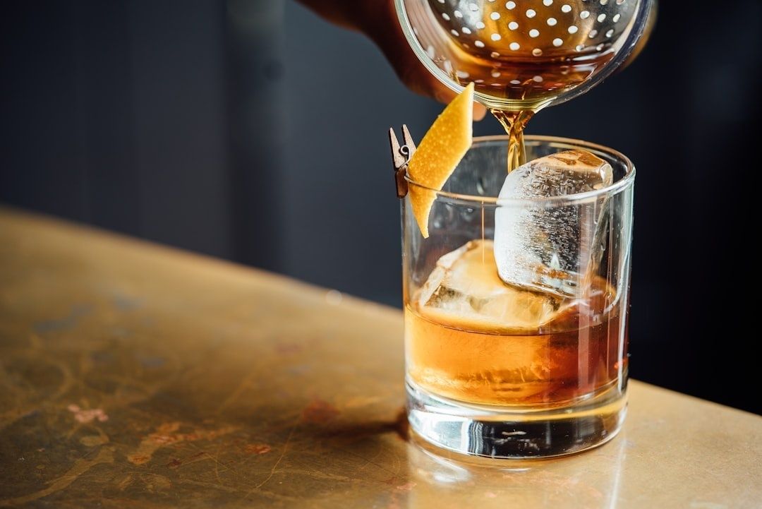 Cocktail med stora iskuber och apelsinzest medan en drink silas över glaset