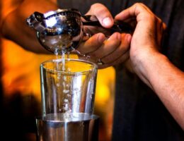 Bartender häller en kyld drink från shaker genom sil till ett glas