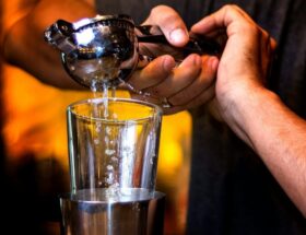 Bartender häller en kyld drink från shaker genom sil till ett glas