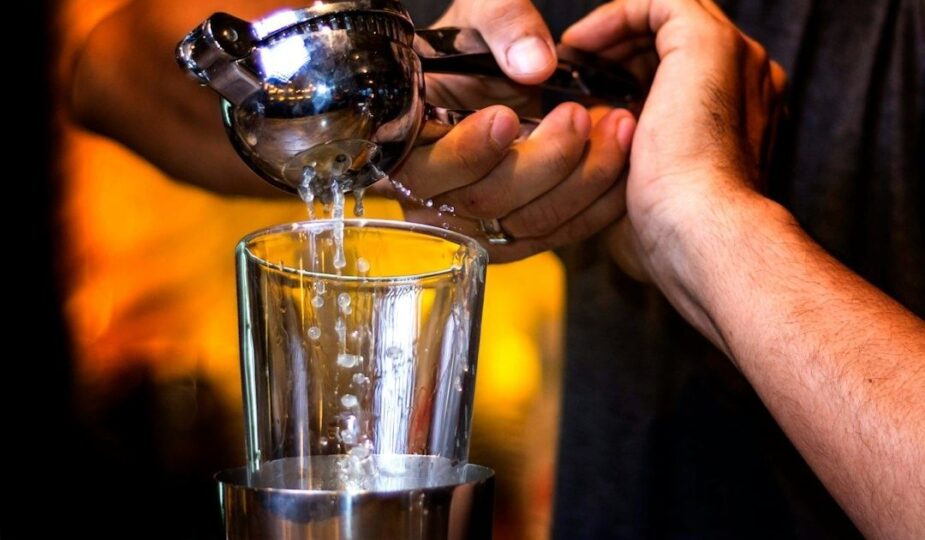 Bartender häller en kyld drink från shaker genom sil till ett glas