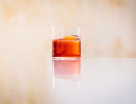 Glas med röd vermouthliknande dryck och apelsinzest på ett bord