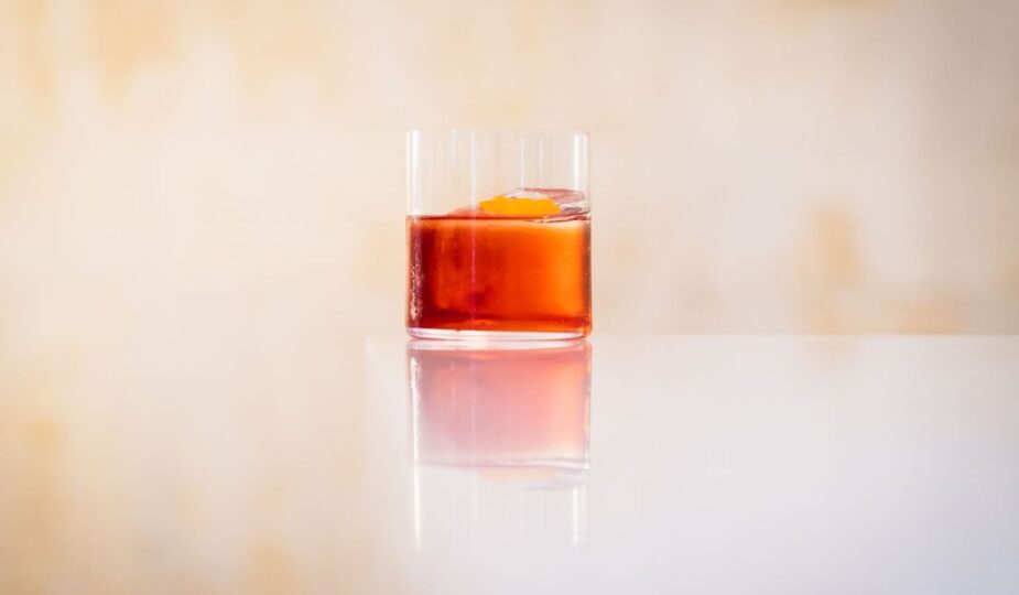 Glas med röd vermouthliknande dryck och apelsinzest på ett bord