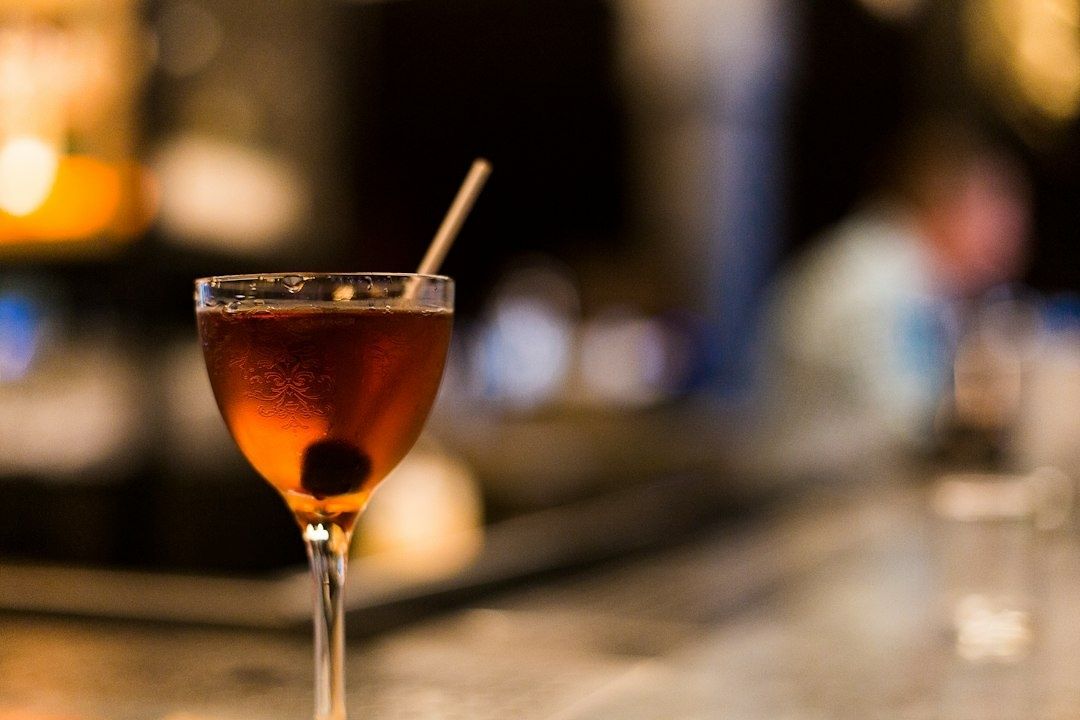 Ett glas bärnstensfärgad vermouth med is och sugrör i en bar